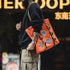 Person holding an orange tote bag with patches against a blurred background